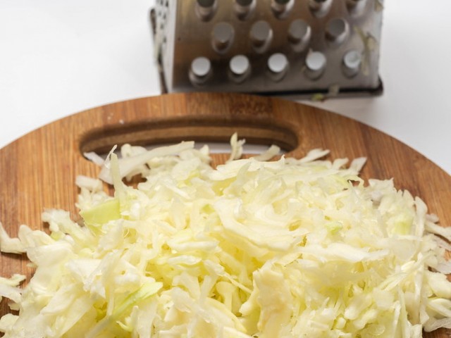 Grated cabbage salad on the round wooden board with metal grater